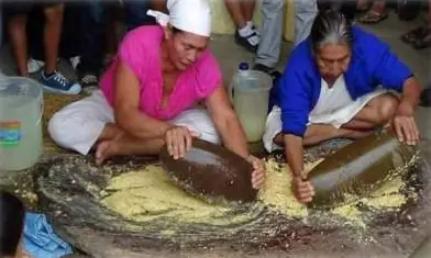 Dos mujeres moliendo maíz sobre una piedra grande