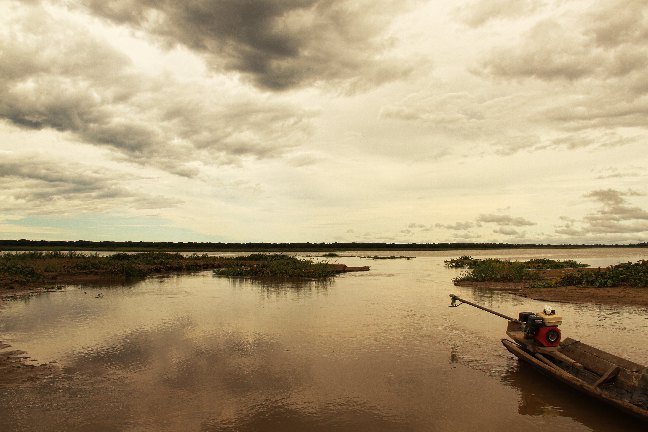 Canoa con motor sobre las aguas color té del Lago Moa bajo un cielo de nubes al atardecer